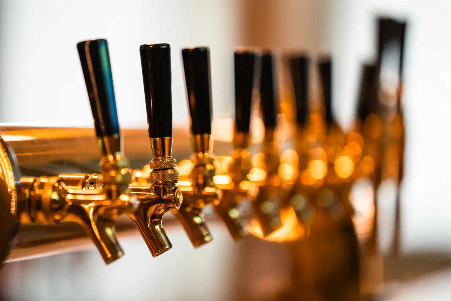 Close-up of polished gold beer taps with black handles lined up on a bar, with a shallow depth of field and warm ambient lighting.